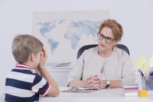 Shot of a schoolboy covering his face with hands during a talk with a head teacher