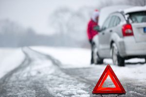 woman checking her car during a snowstorm, safety triangle in foreground