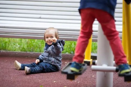 A child watches another child climb on playground equipment.