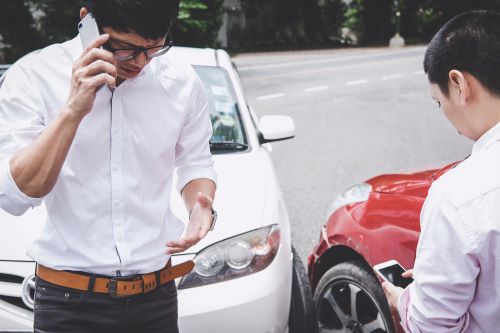 A driver talks on the phone while his passenger waits after a car accident.